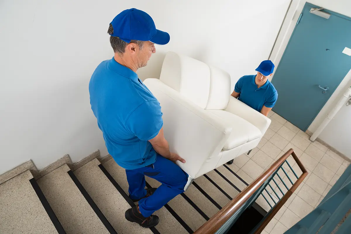 Two delivery guys carrying a sofa up a flight of stairs