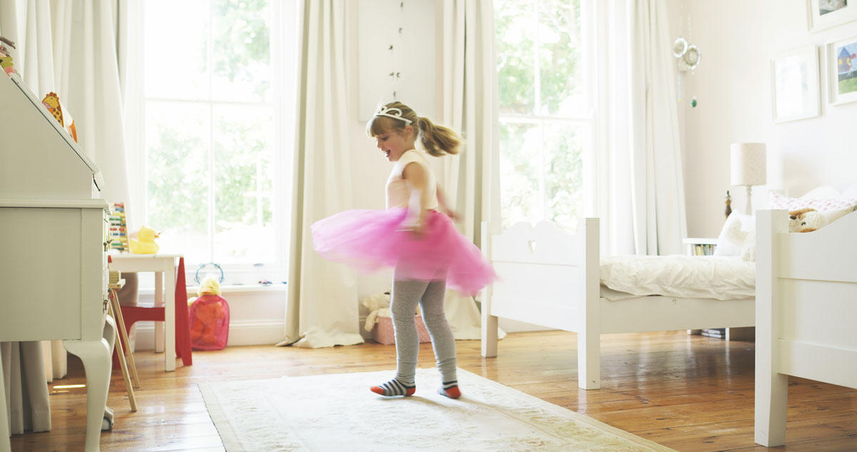 Little girl plays in her bedroom with the new bedding for springtime. 